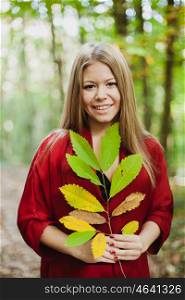 Blonde girl in a misterious forest holding a branch of a tree with autumn colors