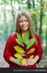 Blonde girl in a misterious forest holding a branch of a tree with autumn colors