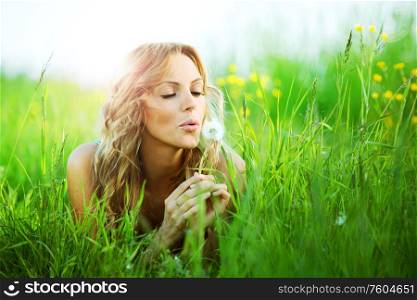 Blonde girl lays on spring meadow and blow on dandelion i wish concept. Girl blow at dandelion i wish
