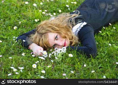 blonde girl lie on the grass and hold flower for garland from daisies, outdoor portrait.