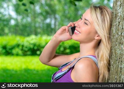 blonde girl on the phone leaning against a tree