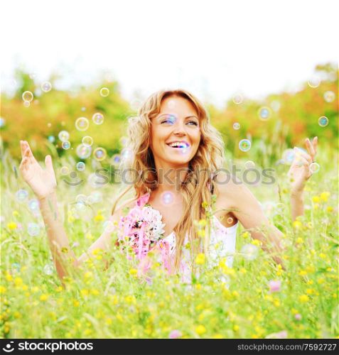 Blonde girl starts soap bubbles and smiling in a green spring field. Girl starts soap bubbles