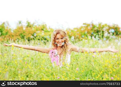Blonde girl starts soap bubbles and smiling in a green spring field. Girl starts soap bubbles