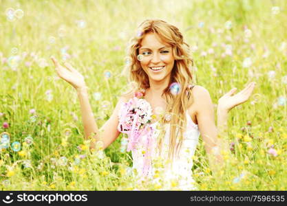 Blonde girl starts soap bubbles and smiling in a green spring field. Girl starts soap bubbles