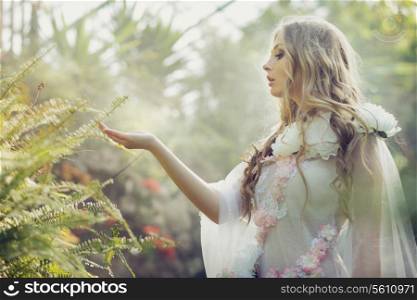 Blonde girl touching the leaves of fern