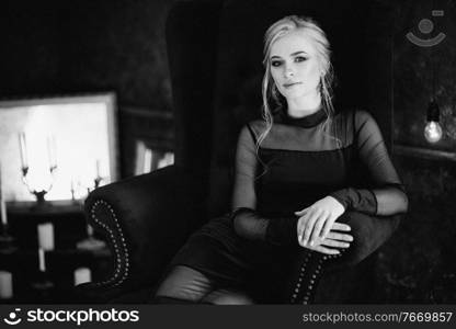 Blonde girl with blue eyes in a black dress in a dark turquoise interior