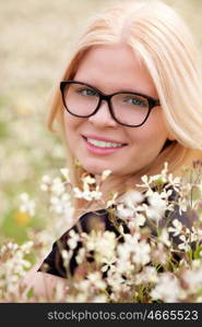 Blonde girl with glasses in the field surrounded by flowers