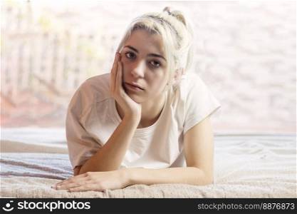 blonde girl with hand on chin stretched out on bed with a sad face