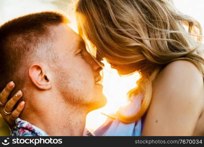 blonde girl with loose hair in a light blue dress and a guy in the light of sunset in nature