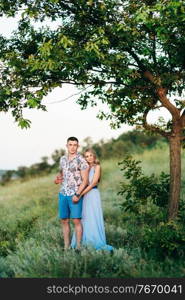 blonde girl with loose hair in a light blue dress and a guy in the light of sunset in nature