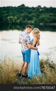 blonde girl with loose hair in a light blue dress and a guy in the light of sunset in nature