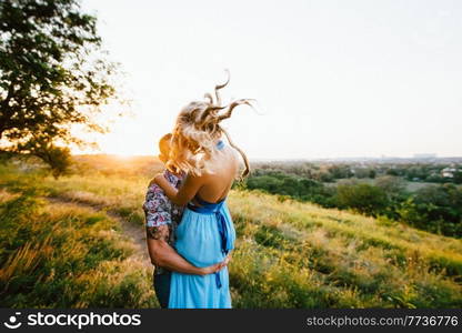 blonde girl with loose hair in a light blue dress and a guy in the light of sunset in nature