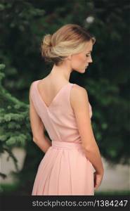 blonde girl with stylish hairstyle in pink dress. portrait of young woman in spring park. side view.. blonde girl with stylish hairstyle in pink dress. portrait of young woman in spring park. side view