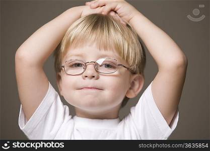 Blonde-haired boy wearing glasses with hands on head