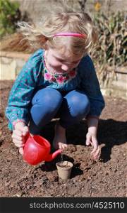 Blonde haired girl watering seeds she has just planted from a toy teapot