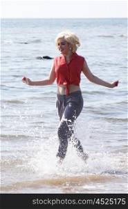 Blonde haired young woman at the beach running through the sea