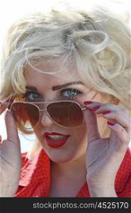 Blonde haired young woman looking over her sunglasses smiling
