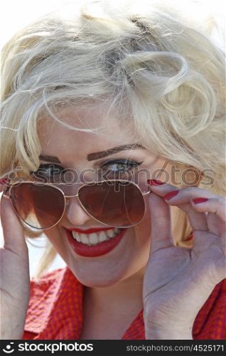 Blonde haired young woman looking over her sunglasses smiling