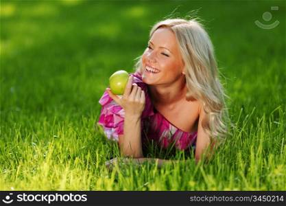 blonde holding an apple in his hand lying on green grass
