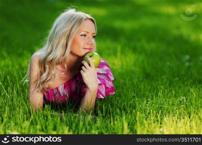 blonde holding an apple in his hand lying on green grass