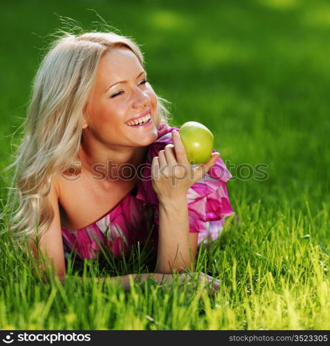 blonde holding an apple in his hand lying on green grass