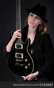 Blonde in a black hat and jacket with guitar in hand