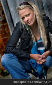 Blonde in denim sits outside disused warehouse
