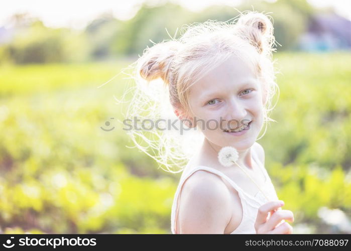 blonde Little girl holding dandelion and blowing it on the Sunset. summer holidays and mood