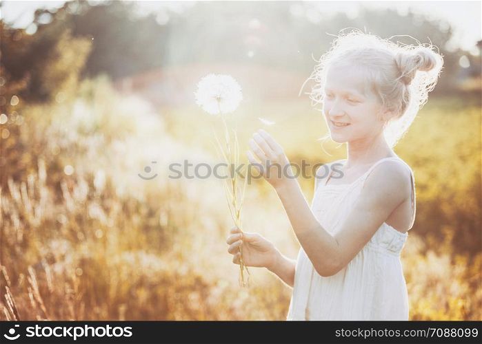 blonde Little girl holding dandelion and blowing it on the Sunset. summer holidays and mood