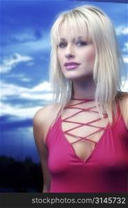 Blonde model poses in the studio wearing a red top and standing against a blue sky.