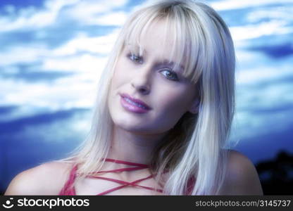 Blonde model poses in the studio wearing a red top and standing against a blue sky.