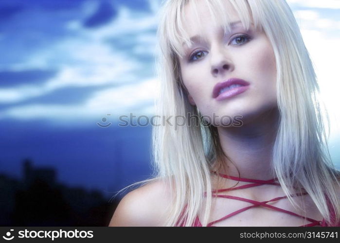 Blonde model poses in the studio wearing a red top and standing against a blue sky.