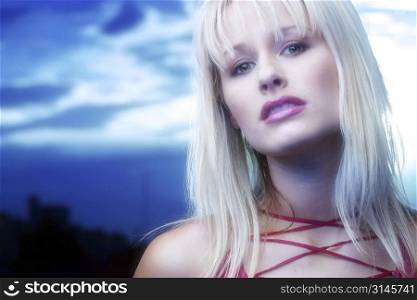 Blonde model poses in the studio wearing a red top and standing against a blue sky.