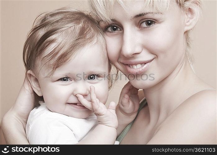 Blonde mother holds baby with hand in mouth