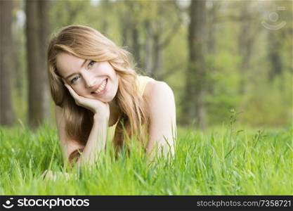Blonde pretty girl laying on the grass in spring park and smiling. Girl laying on the grass