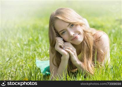 Blonde pretty girl laying on the grass in spring park and smiling. Girl laying on the grass