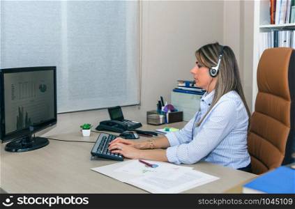 Blonde secretary with headset working with computer in office. Blonde secretary working with computer in office