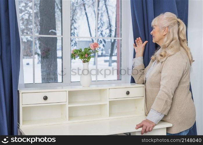 blonde senior woman looking through window home