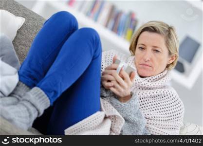 blonde sick woman laying on the couch with mug
