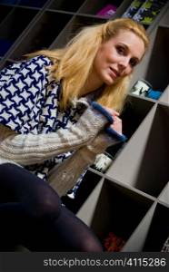 Blonde sits on chair beside bookcase in patterned jumper dress