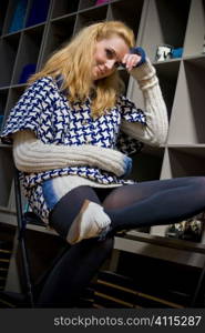 Blonde sits on chair beside bookcase in patterned jumper dress