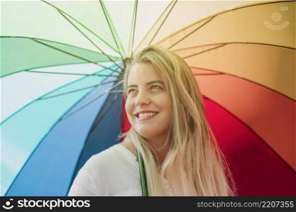 blonde smiling young woman holding rainbow umbrella
