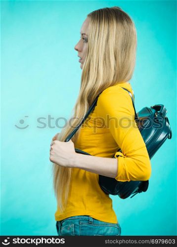 Blonde teenage girl going to school or college wearing stylish backpack. Outfit trendy accessories. On blue. Teen girl with school backpack