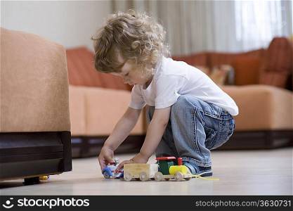 Blonde toddler playing with toy train on floor