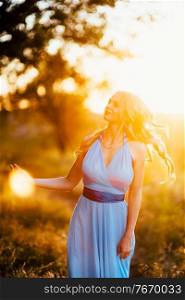 blonde with loose hair in a light blue dress in the light of sunset in nature