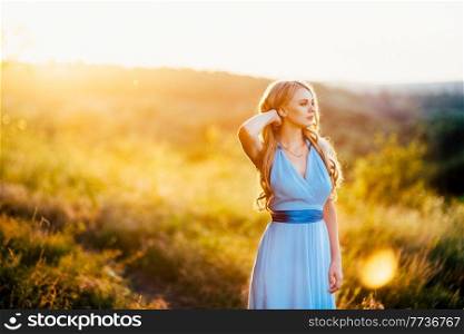 blonde with loose hair in a light blue dress in the light of sunset in nature