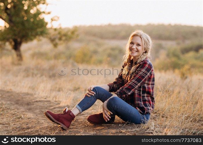 blonde with pigtails in a shirt, jeans, red shoes smiling at sunset