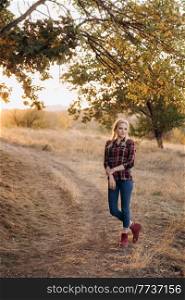blonde with pigtails in a shirt, jeans, red shoes smiling at sunset