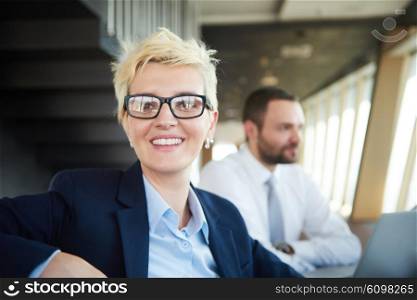 blonde with short hairstyle and glasses, business woman on meeting, people group in background at modern bright office indoors