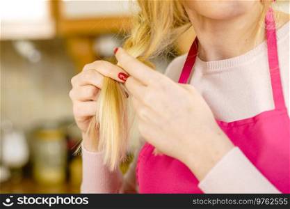 Blonde woman creating her hairstyle, making braid wearing apron. Lovely female getting ready. Waitress, chef getting ready to work. Woman making braid on blonde hair